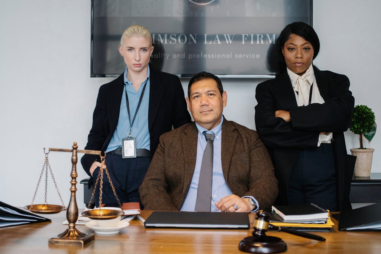 Diverse law firm employees in suits at a desk. Scale and gavel signify justice.